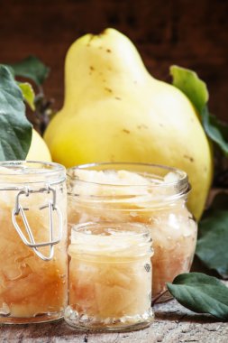 Pink quince jam in glass jars and fresh quince fruits with leaves 