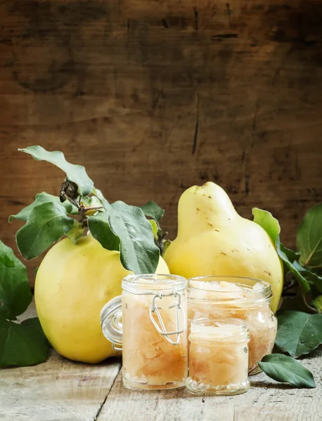 Pink quince jam in glass jars and fresh quince fruits with leaves 