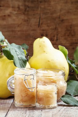 Pink quince jam in glass jars and fresh quince fruits with leaves 