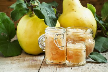 Pink quince jam in glass jars and fresh quince fruits with leaves 