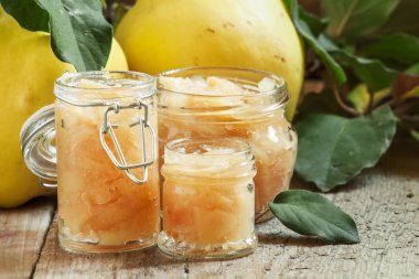 Pink quince jam in glass jars and fresh quince fruits with leaves 
