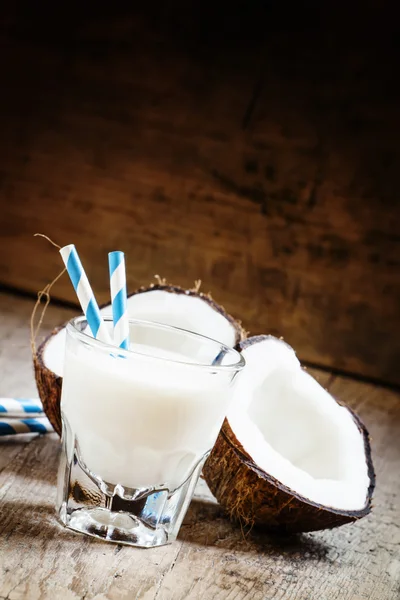 Кокосовое молоко в стакане с полосатыми соломинками и кокосовыми половинками — стоковое фото