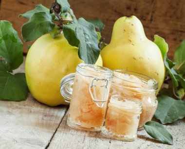 Pink quince jam in glass jars and fresh quince fruits with leaves 