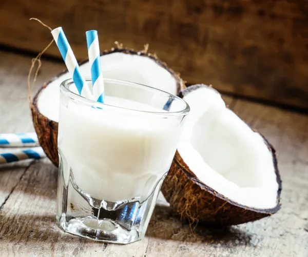 Kokosmilch im Glas mit gestreiften Strohhalmen und Kokosnusshälften — Stockfoto