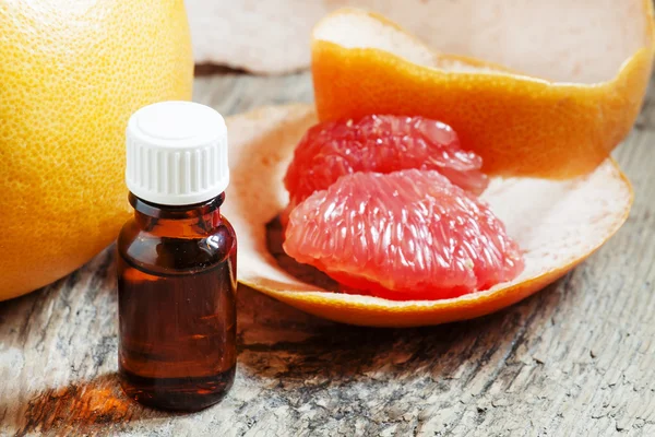 Aceite esencial de pomelo en una botella pequeña y pomelo fresco —  Fotos de Stock