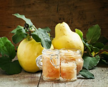 Pink quince jam in glass jars and fresh quince fruits with leaves 