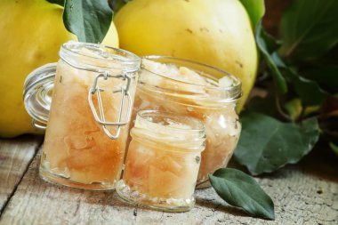 Pink quince jam in glass jars and fresh quince fruits with leaves 