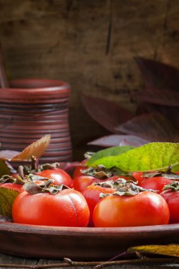 Ripe persimmons with leaves on a clay plate 