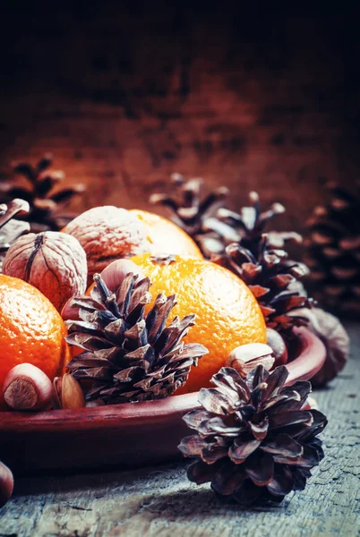 Глиняная тарелка с апельсиновыми мандаринами, еловыми шишками, грецкими орехами, фундуками и фисташками — стоковое фото