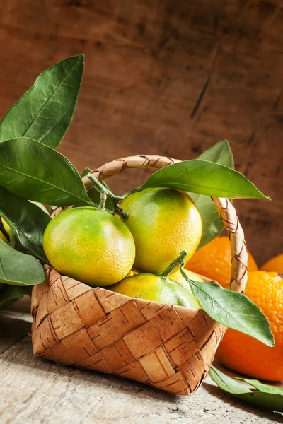 Mandarines fraîches avec des feuilles dans un panier en osier et des oranges — Photo