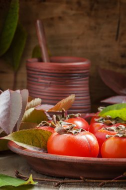 Ripe persimmons with leaves on a clay plate 