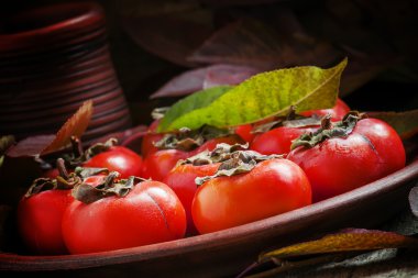 Ripe persimmons with leaves on a clay plate