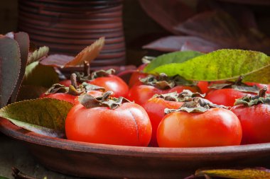 Ripe persimmons with leaves on a clay plate