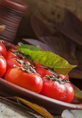Ripe persimmons with leaves on a clay plate