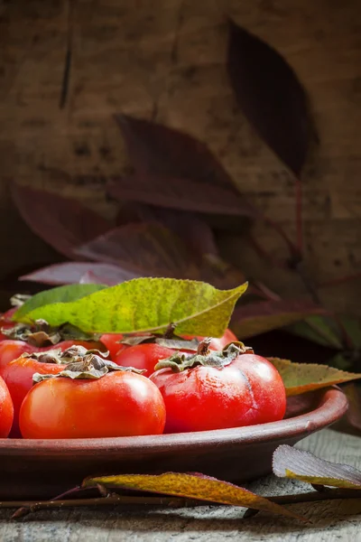 Ripe persimmons with leaves on a clay plate — Stok fotoğraf