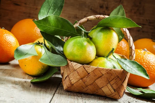 Vers mandarijnen met bladeren in een rieten mand en sinaasappelen — Stockfoto