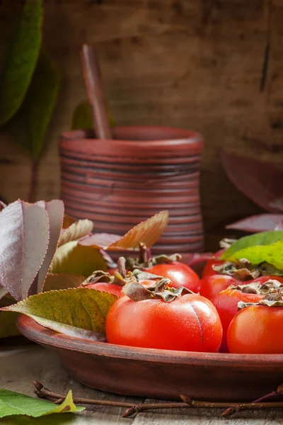 Ripe persimmons with leaves on a clay plate — Stok fotoğraf