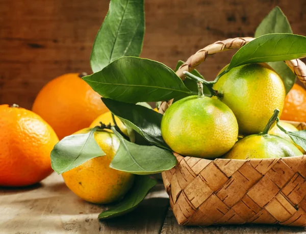 Mandarini freschi con foglie in un cesto di vimini e arance — Foto Stock