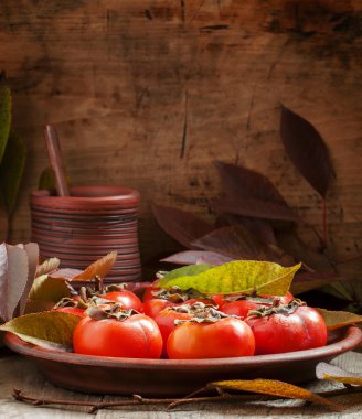 Ripe persimmons with leaves on a clay plate