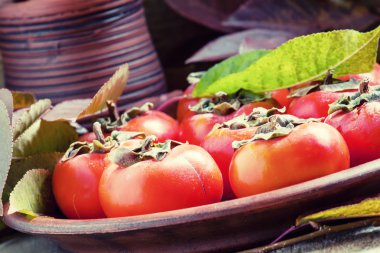 Ripe persimmons with leaves on a clay plate