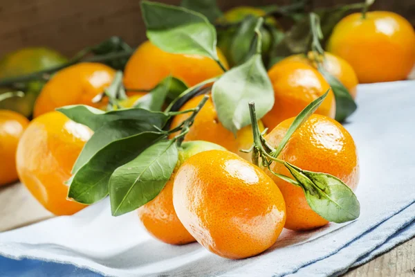 Verse rijpe mandarijnen met groene bladeren op een blauw servet — Stockfoto