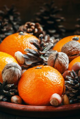 Clay plate with orange mandarins, fir cones, walnuts, hazelnuts and pistachios 