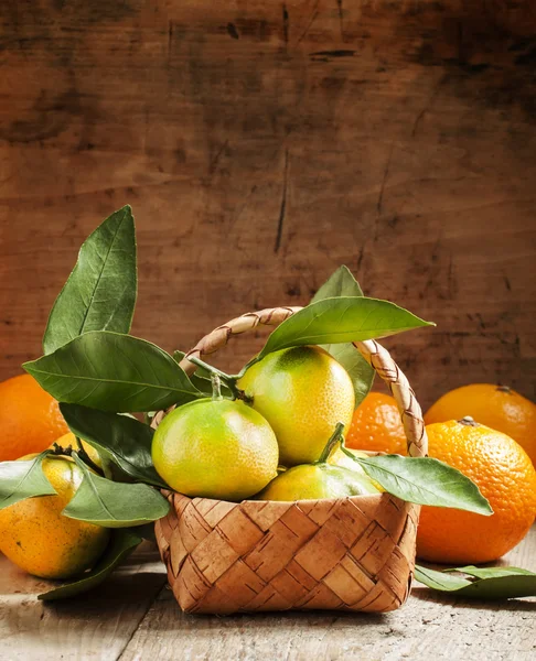 Mandarines fraîches avec des feuilles dans un panier en osier et des oranges — Photo