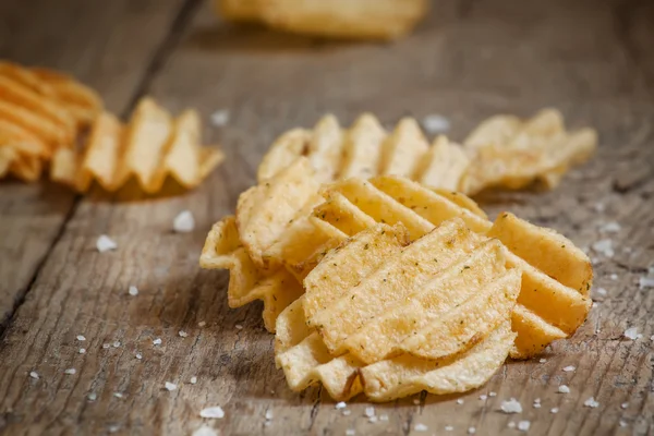 Golden corrugated potato chips on an old wooden table — ストック写真