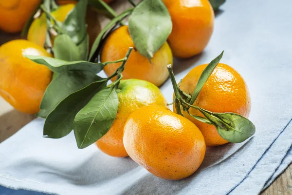 Świeżych dojrzałych mandarynki z zielonych liści na serwetce niebieski — Zdjęcie stockowe