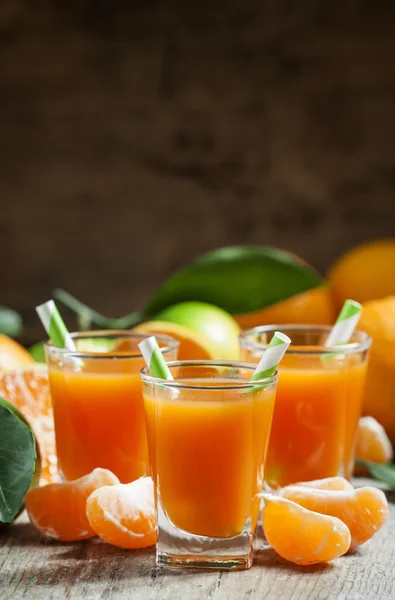 Свежий сок спелых мандаринов в маленьких стаканах с полосатыми соломинками — стоковое фото