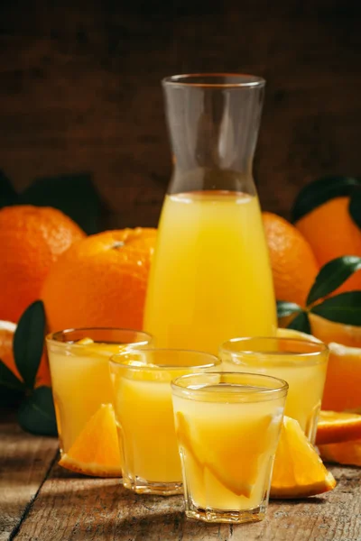Orange juice with fruit pieces in small cups and a jug — Stock Photo, Image