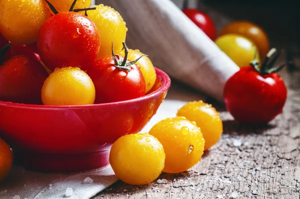 Tomates cherry rojos y anaranjados en un bol rojo — Foto de Stock