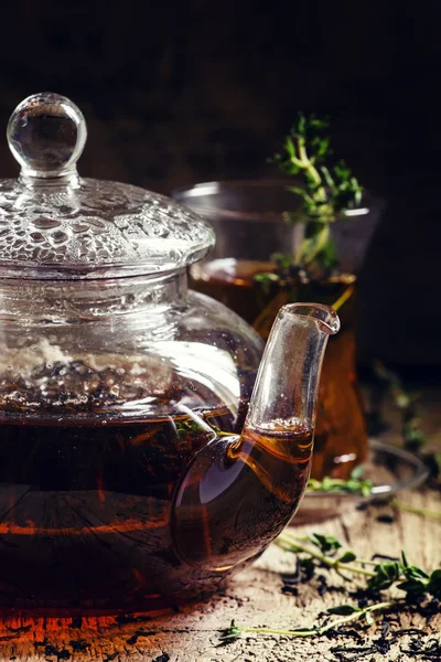 Glass teapot with black tea with thyme — Stock Photo, Image