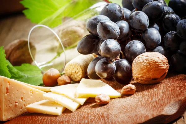 Sýr, modré hrozny, vinné révy, ořechy a sklenice — Stock fotografie