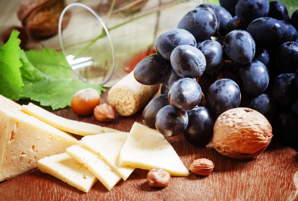 Sýr, modré hrozny, vinné révy, ořechy a sklenice — Stock fotografie