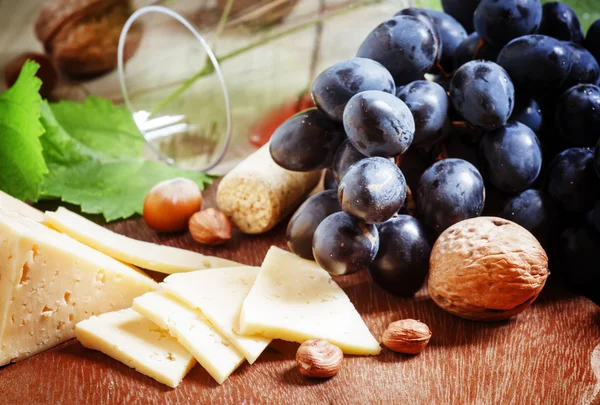 Fromage, raisins bleus, vigne, noix et un verre — Photo