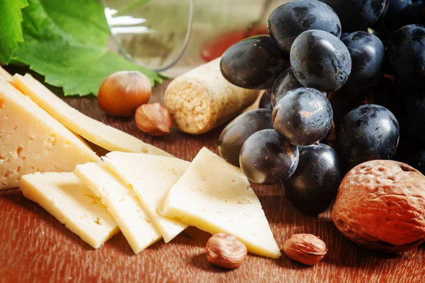 Fromage, raisins bleus, vigne, noix et un verre — Photo