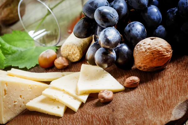 Una copa de vino, rodajas de queso, frutos secos y uvas — Foto de Stock