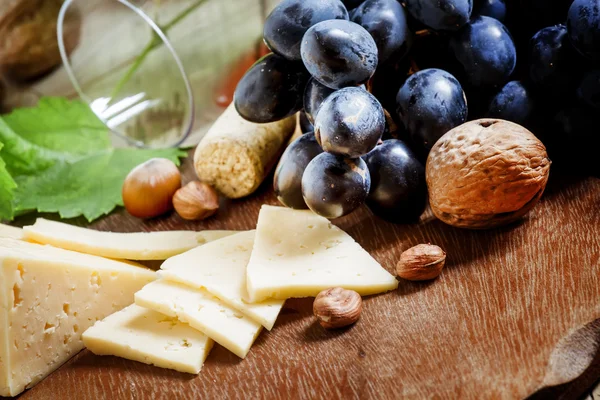 Un bicchiere di vino, fette di formaggio, noci e uva — Foto Stock