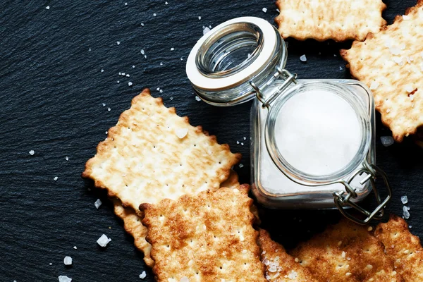 Galletas saladas y sal sobre un fondo oscuro —  Fotos de Stock