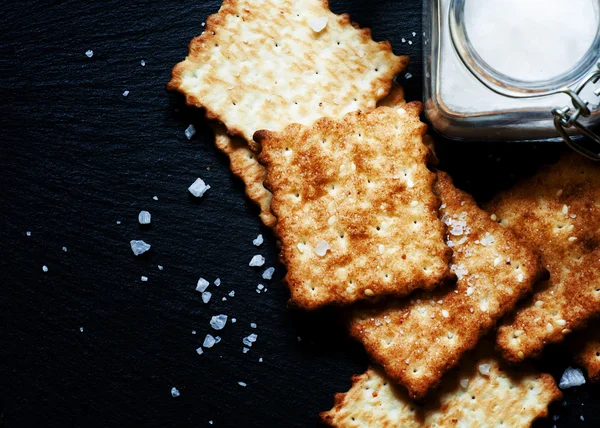 Biscoitos salgados e sal em um fundo escuro — Fotografia de Stock