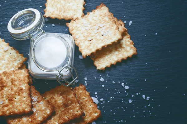 Saltine krakersy i soli na ciemnym tle — Zdjęcie stockowe