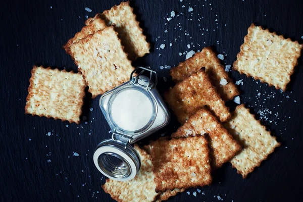 Saltine krakersy i soli na ciemnym tle — Zdjęcie stockowe