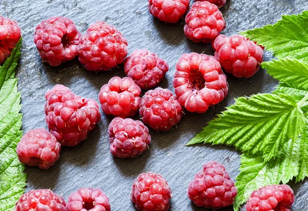Juicy ripe raspberries with leaves on a dark stone background — Stock Photo, Image