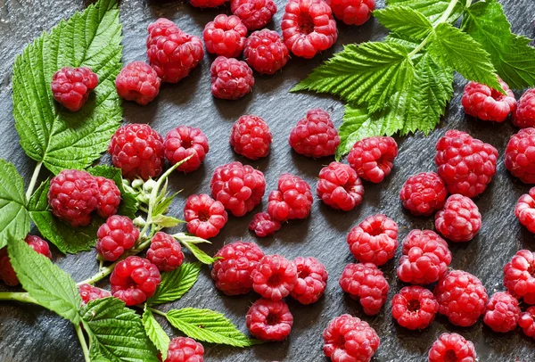 Juicy ripe raspberries with leaves on a dark stone background — Stock Photo, Image