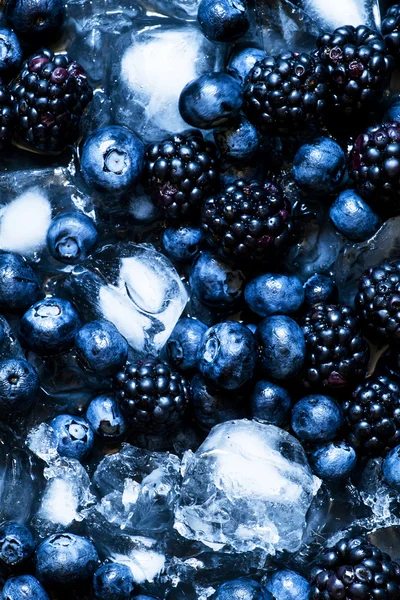 Blackberries and blueberries in ice on a dark background — Stock Photo, Image