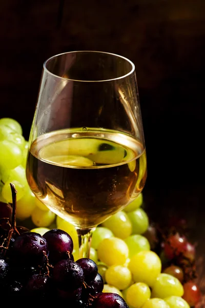 Vitt vin i ett glas och gröna och röda druvor i en flätad korg — Stockfoto