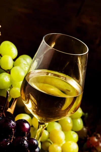 Witte wijn in een glas en groene en rode druiven in een rieten mand — Stockfoto