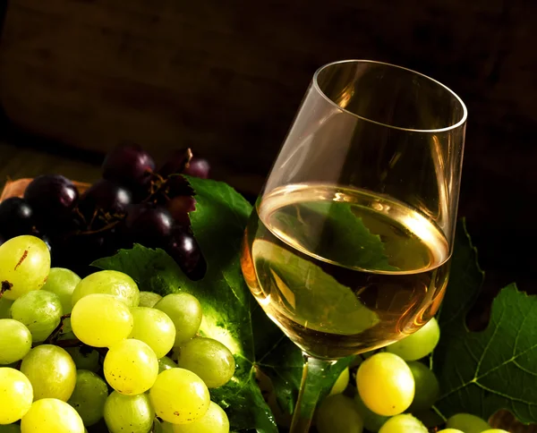 Vinho branco e uvas verdes numa cesta de vime numa adega — Fotografia de Stock