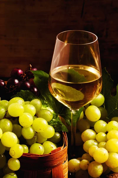 Vinho branco e uvas verdes numa cesta de vime numa adega — Fotografia de Stock